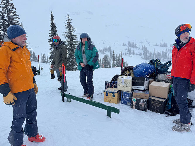 people in ski clothing with bags waiting on helicopter