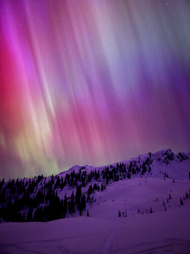 northern lights in purples and greens over a snowy ridge