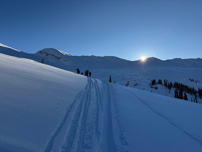 skiers talking on a snowy hill with sun rising over the ridge